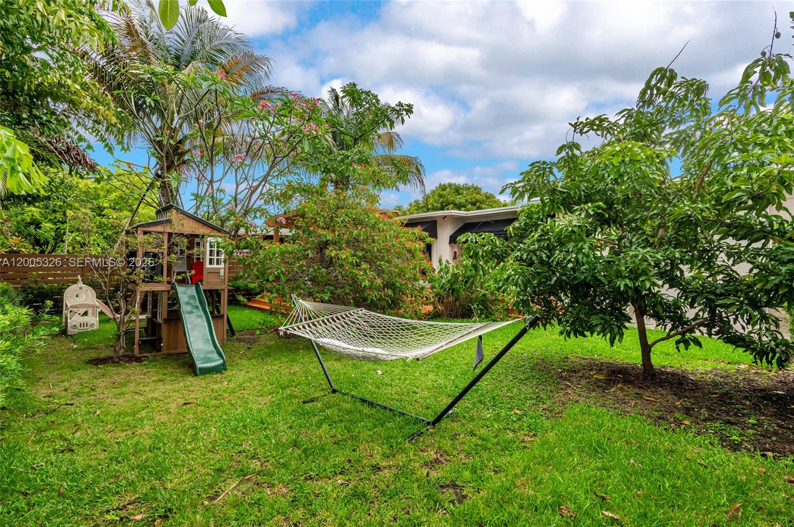 A backyard features a wooden play set with a green slide and a hammock — 9048 Carlyle Ave, Surfside FL 33154, SURFSIDE, FL