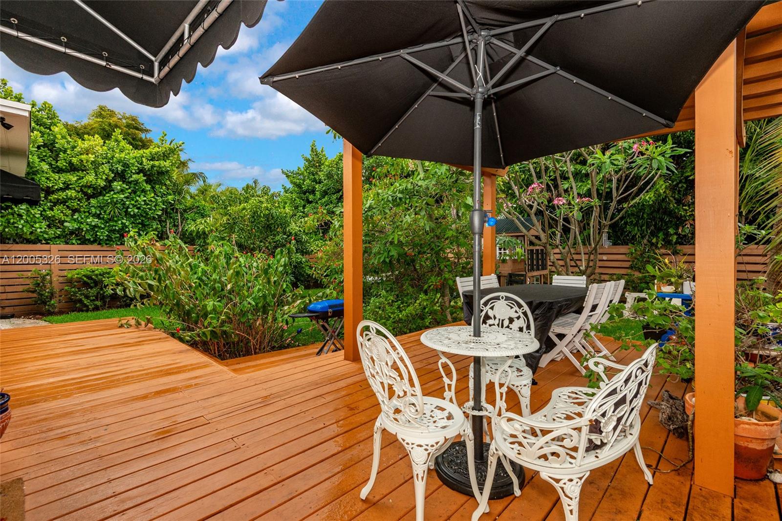 A wooden deck features a patio table with white chairs under a black umbrella — 9048 Carlyle Ave, Surfside FL 33154, SURFSIDE, FL
