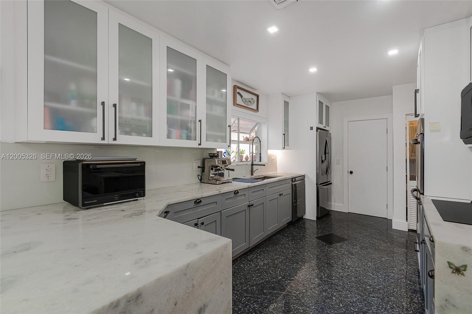 A kitchen features white upper cabinets, gray lower cabinets, marble countertops, and dark flooring — 9048 Carlyle Ave, Surfside FL 33154, SURFSIDE, FL