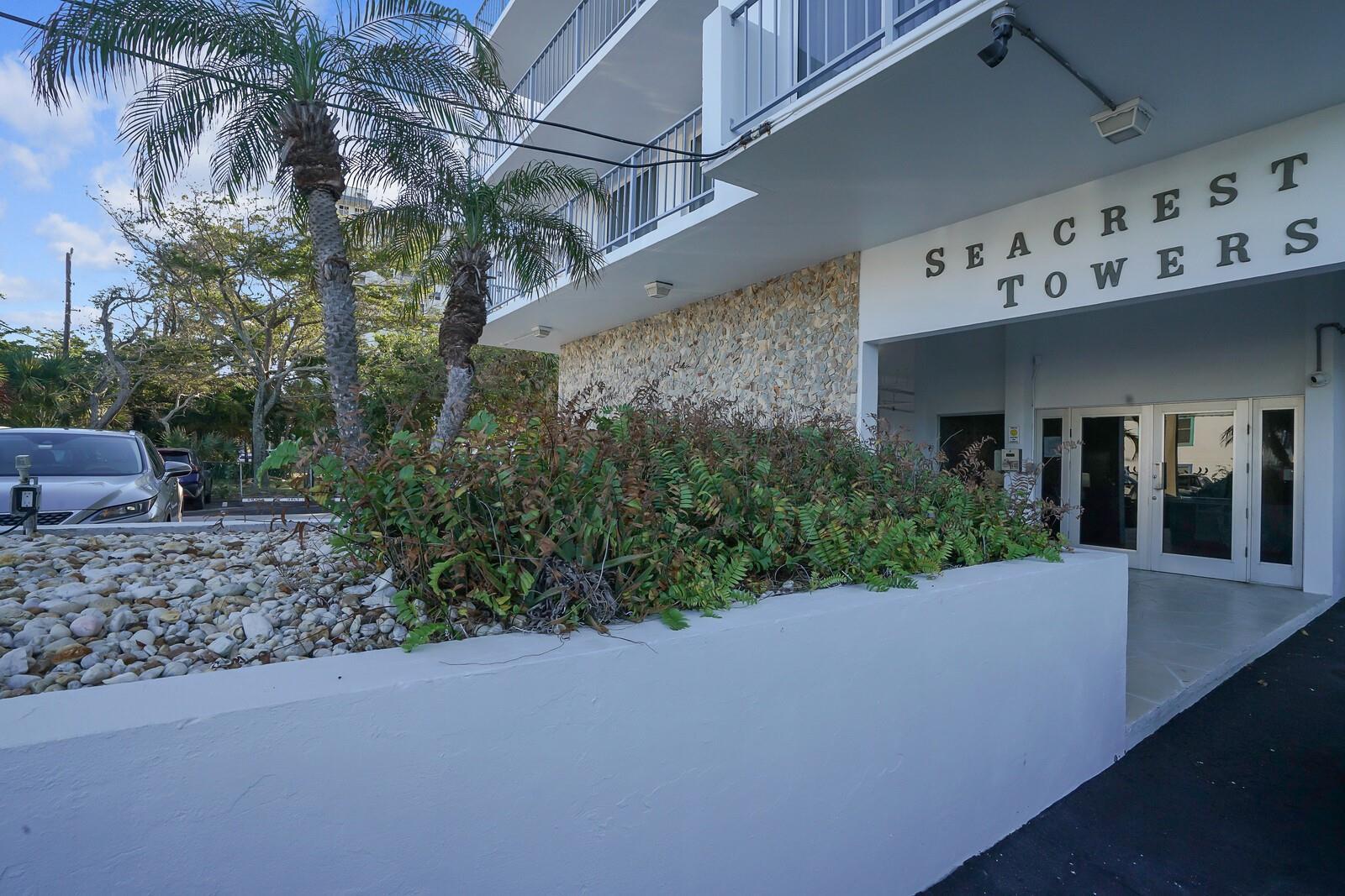 The exterior of Seacrest Towers features a stone-accented wall, landscaping, and a glass-door entrance — 1609 N Riverside Drive # 304, Pompano Beach FL 33062, POMPANO BEACH, FL