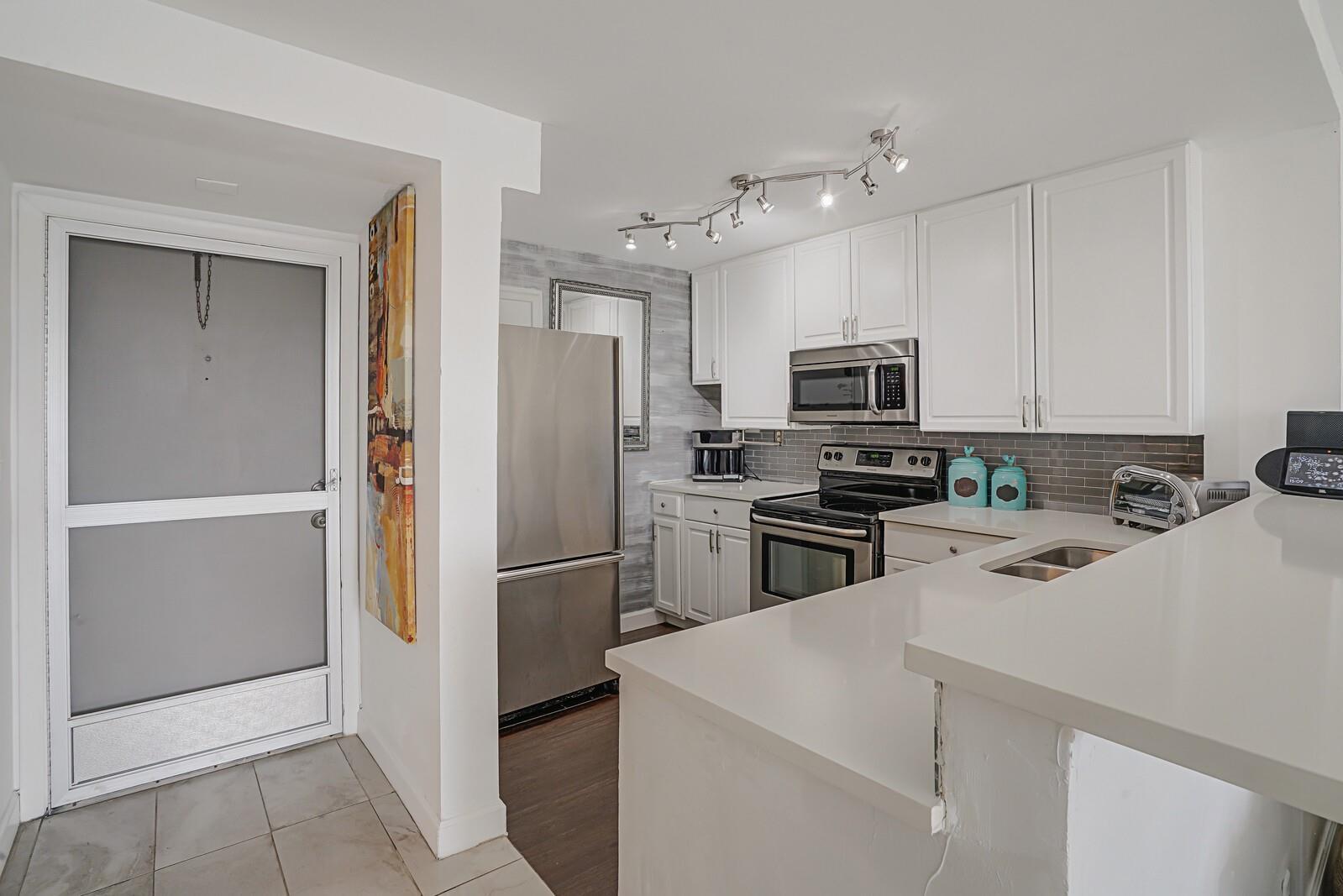 A kitchen features white cabinetry, stainless steel appliances, a gray backsplash, and a white countertop — 1609 N Riverside Drive # 304, Pompano Beach FL 33062, POMPANO BEACH, FL