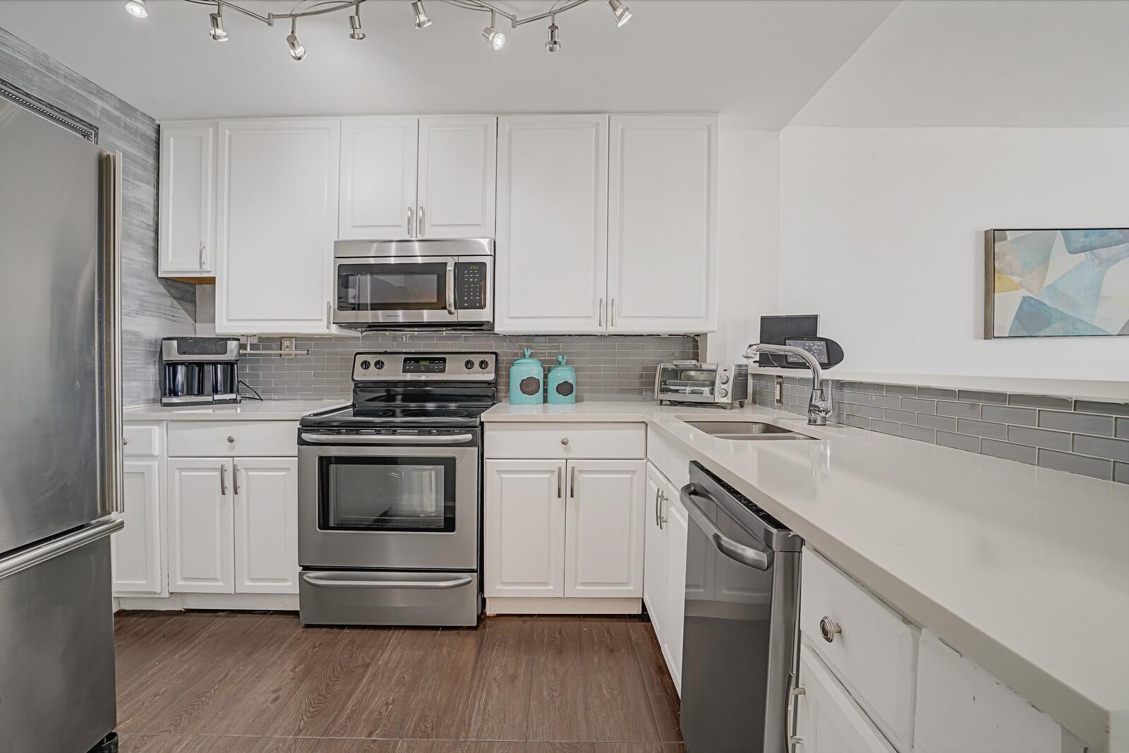 A kitchen features white cabinets, stainless steel appliances, gray subway tile, and wood-look flooring — 1609 N Riverside Drive # 304, Pompano Beach FL 33062, POMPANO BEACH, FL