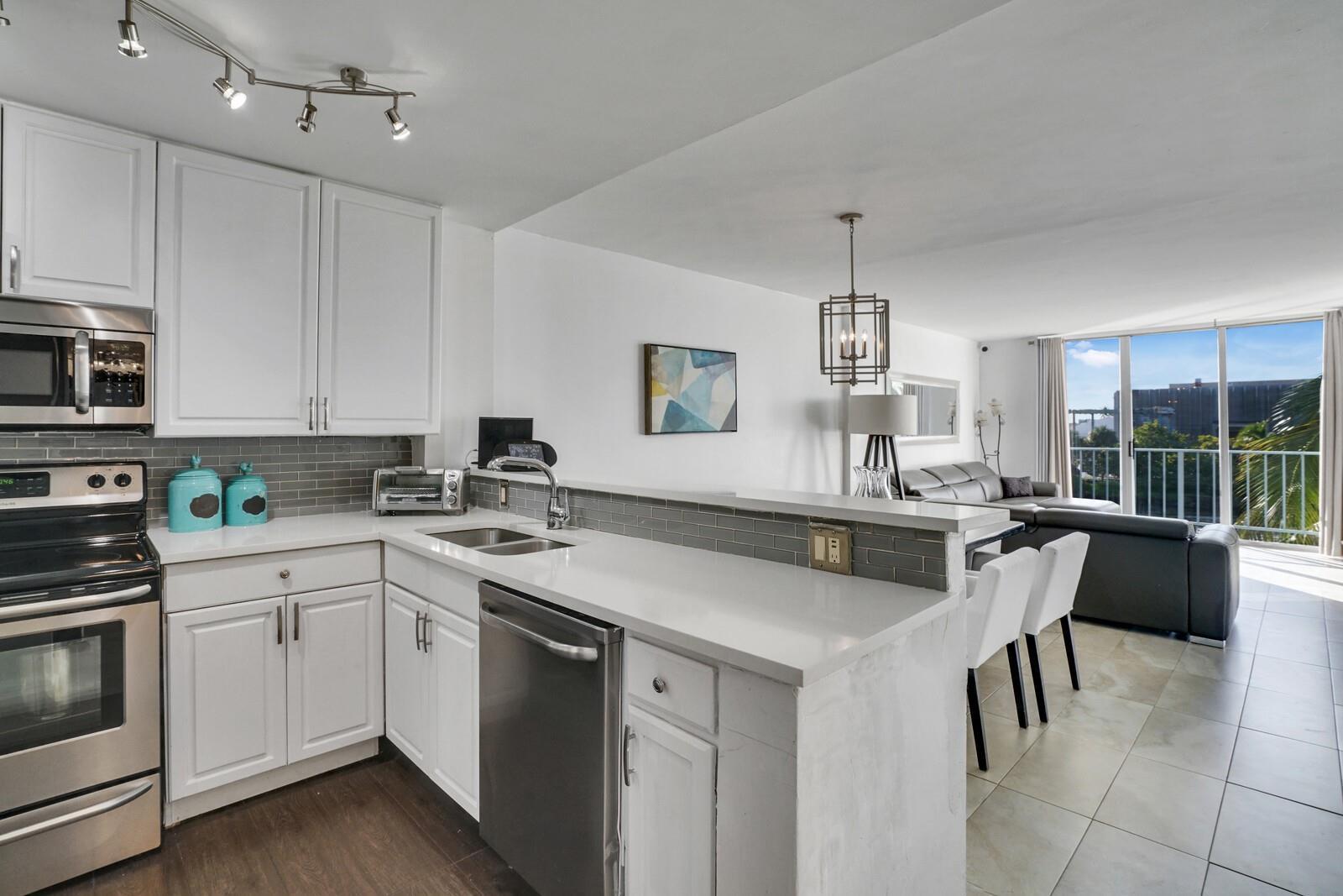A modern kitchen with white cabinets and stainless steel appliances opens to a living area — 1609 N Riverside Drive # 304, Pompano Beach FL 33062, POMPANO BEACH, FL