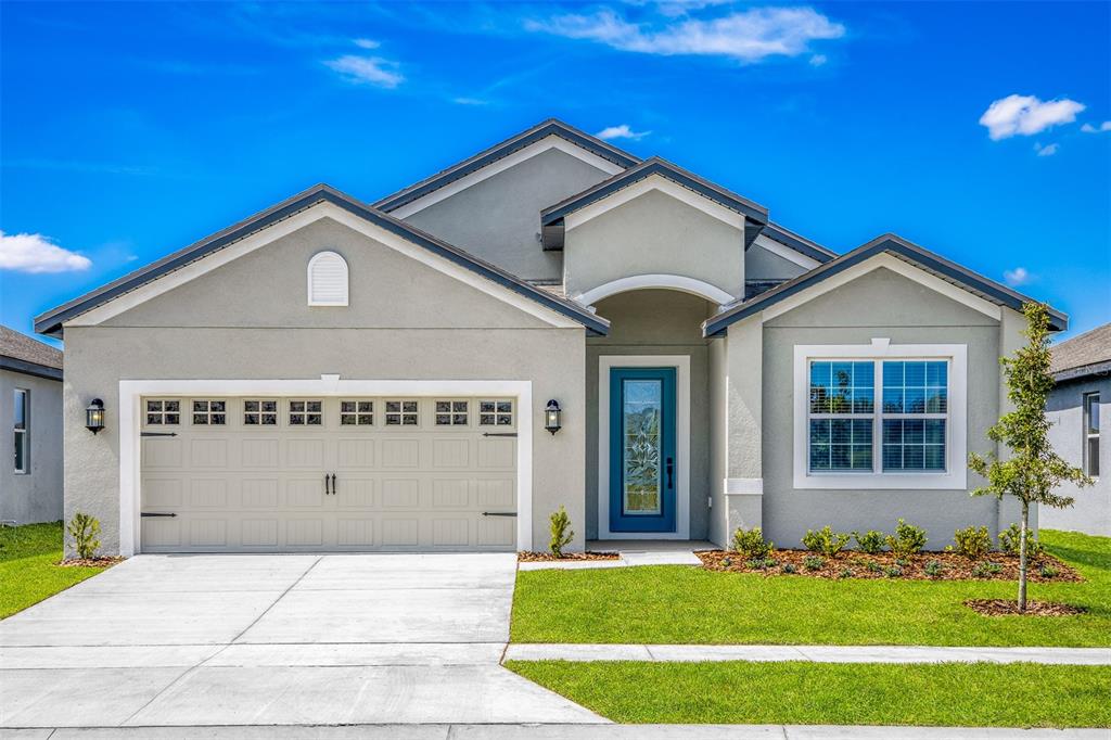 A single-story house with a gray stucco exterior, a two-car garage, and a blue front door — 3352 CHINOTTO DRIVE, LAKE ALFRED, FL