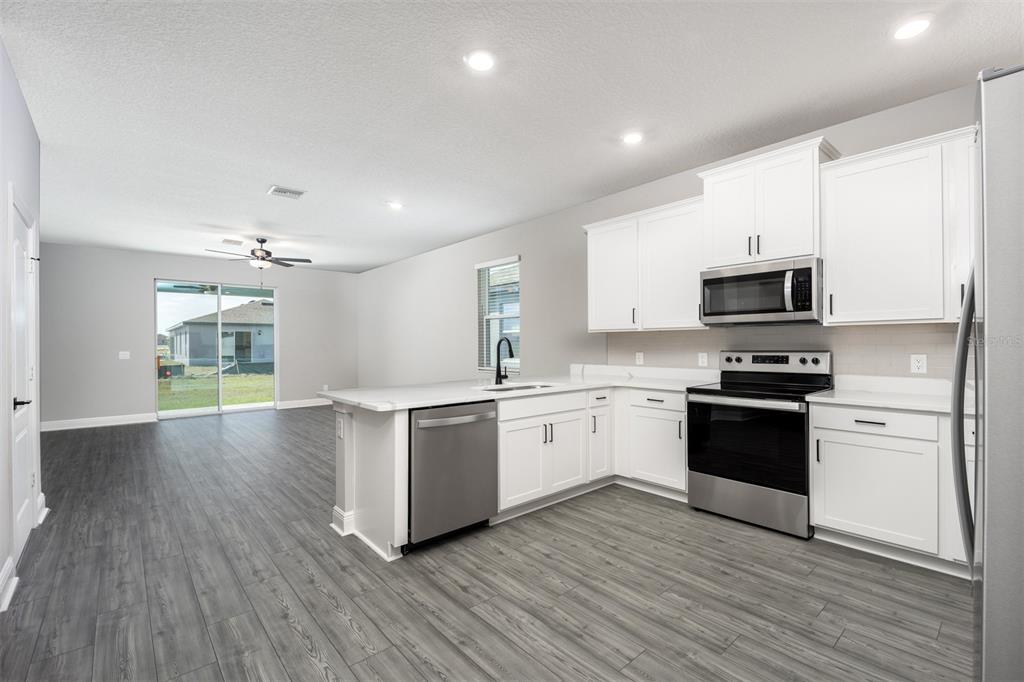 A modern kitchen with white cabinets, stainless steel appliances, and an island overlooks a living area — 3352 CHINOTTO DRIVE, LAKE ALFRED, FL