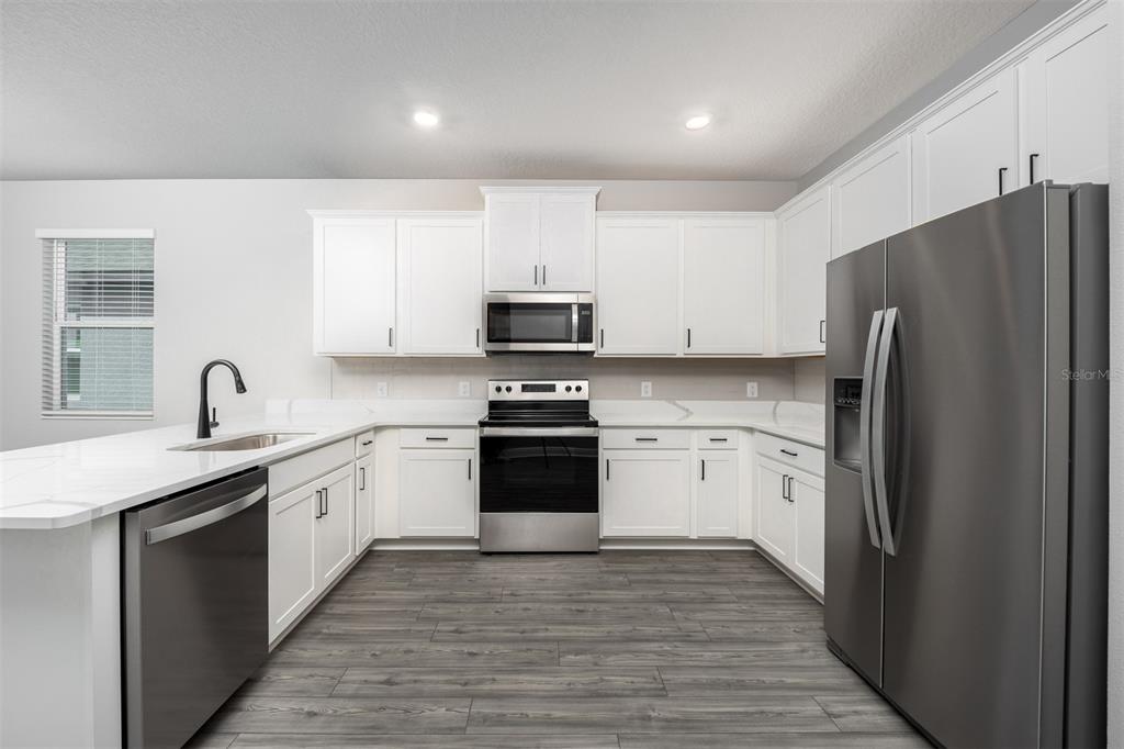 A modern kitchen features white cabinetry, stainless steel appliances, and light-colored countertops — 3352 CHINOTTO DRIVE, LAKE ALFRED, FL