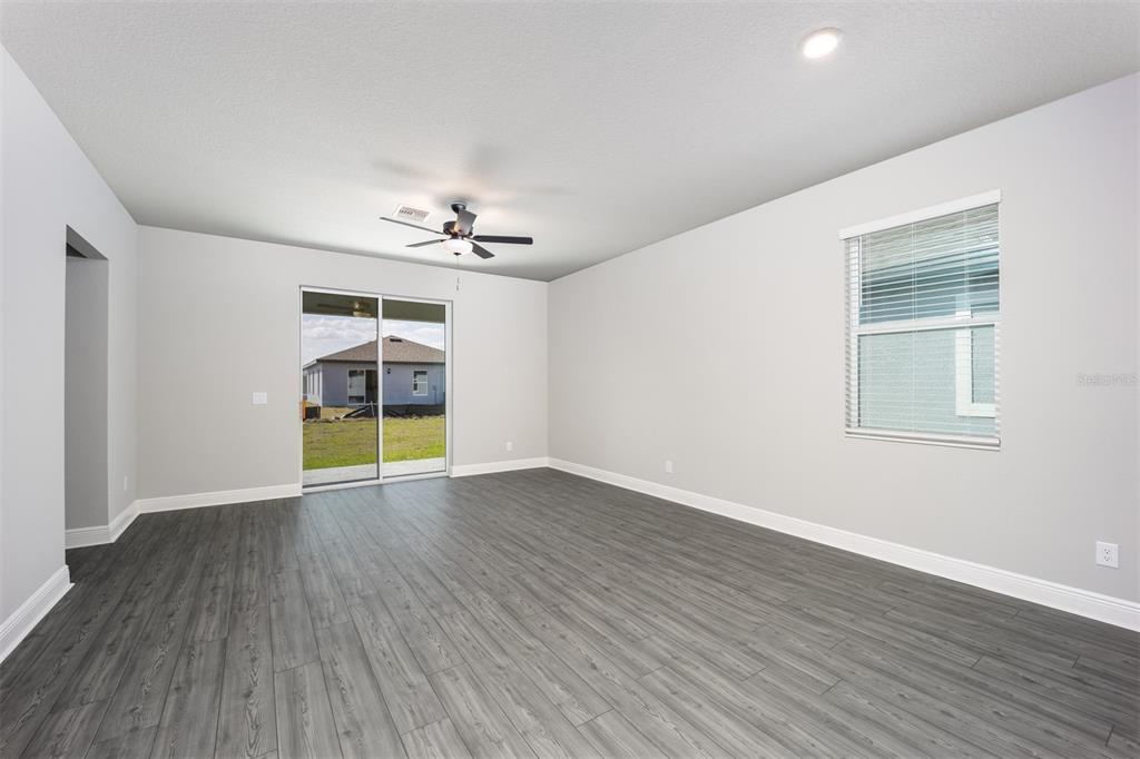 An empty living room features gray wood-look flooring, light gray walls, and a sliding glass door — 3352 CHINOTTO DRIVE, LAKE ALFRED, FL