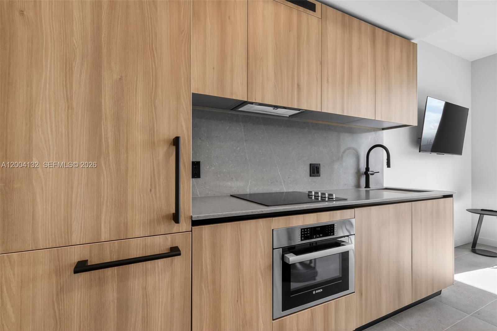 A modern kitchen features light wood cabinetry, a gray stone backsplash, and stainless steel appliances — 121 NE 5th Steet # 3313, Miami FL 33132, MIAMI, FL