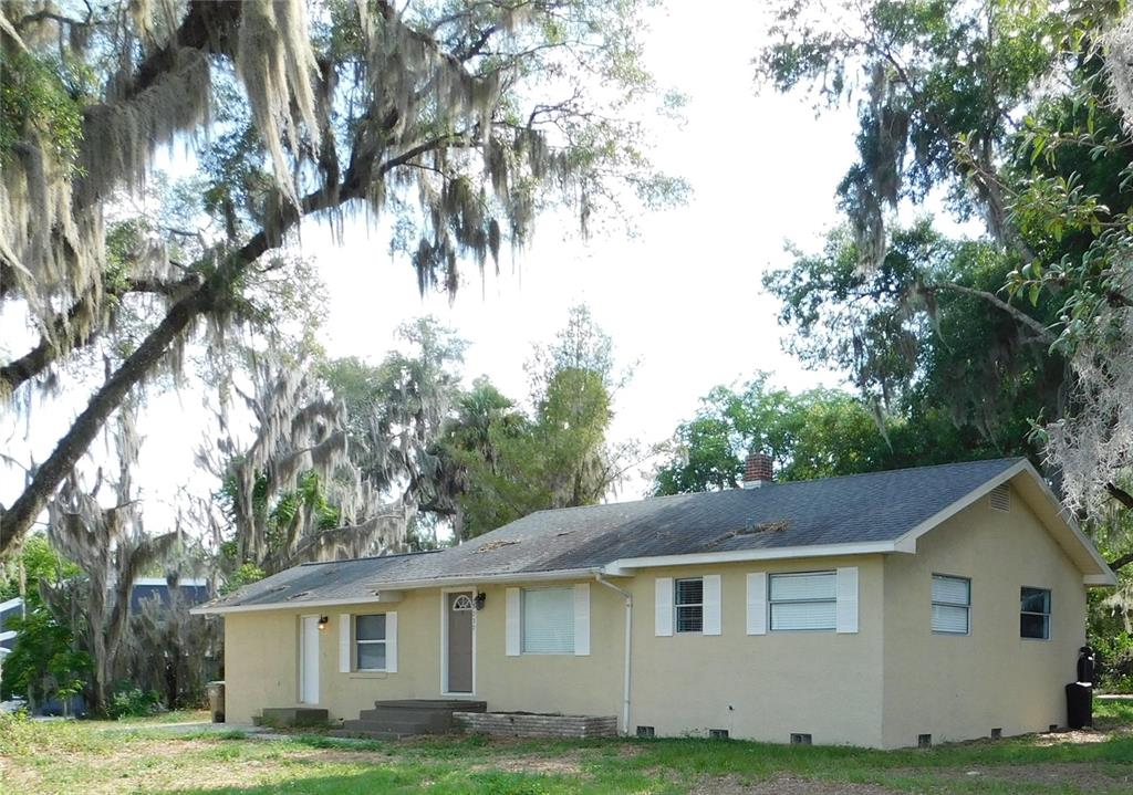 A single-story tan house with a gray roof sits among trees draped in Spanish moss — 7237 HILLCREST STREET, LEESBURG, FL
