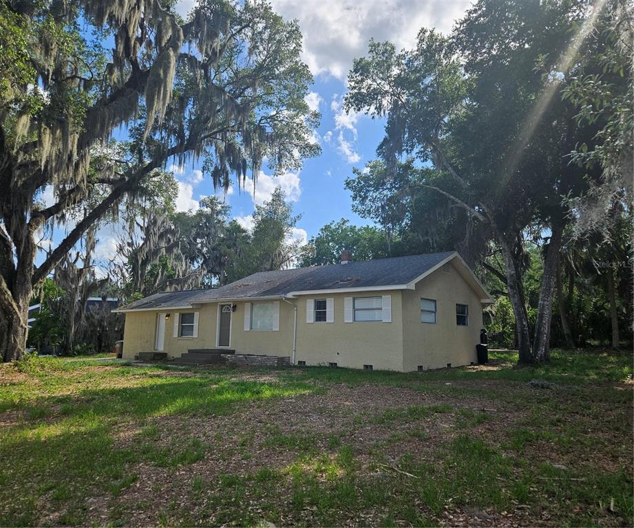 A single-story yellow house with a shingled roof sits on a grassy lot with trees — 7237 HILLCREST STREET, LEESBURG, FL