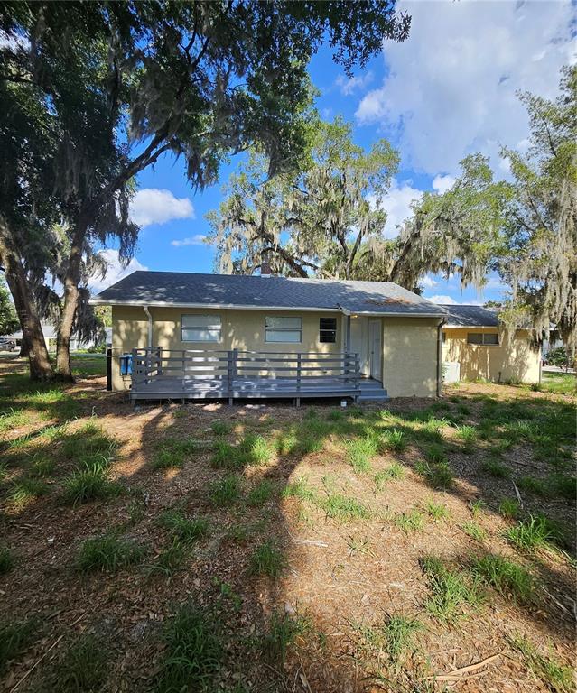 A single-story house with a gray wooden deck and large oak trees in the yard — 7237 HILLCREST STREET, LEESBURG, FL