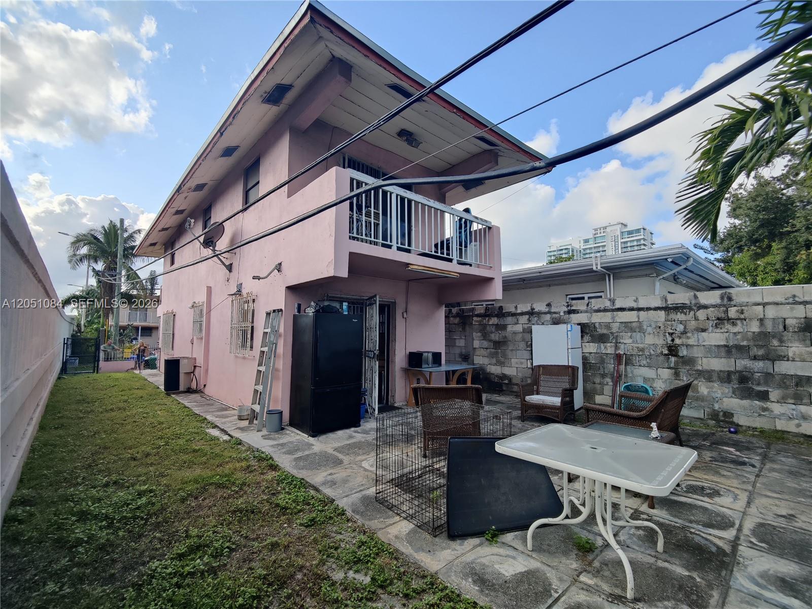 The exterior of a two-story pink house features a balcony, patio, and a stone wall — 945 NW 19th Ave, Miami FL 33125, MIAMI, FL