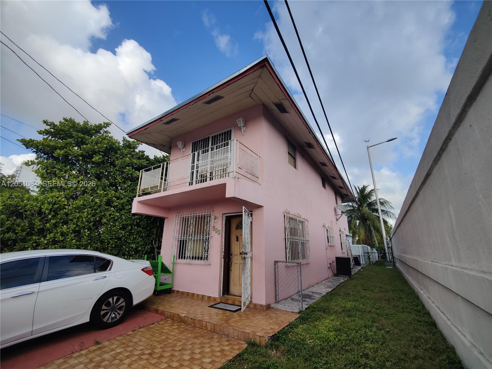 A two-story pink house features a balcony, security bars on windows, and a tiled porch — 945 NW 19th Ave, Miami FL 33125, MIAMI, FL