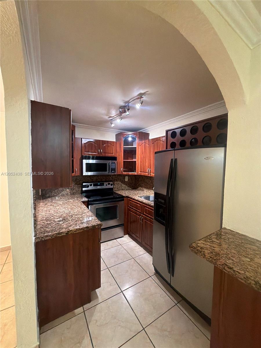 A kitchen features dark wood cabinets, granite countertops, stainless steel appliances, and tile flooring — 1101 SW 122nd Ave # 106, Miami FL 33184, MIAMI, FL