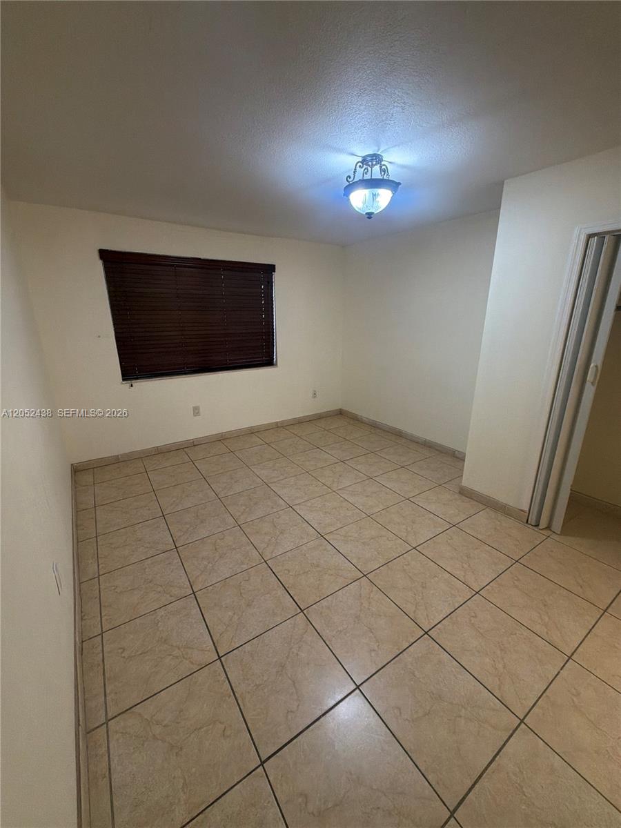 An empty bedroom features beige tile flooring, white walls, and a ceiling light fixture — 1101 SW 122nd Ave # 106, Miami FL 33184, MIAMI, FL