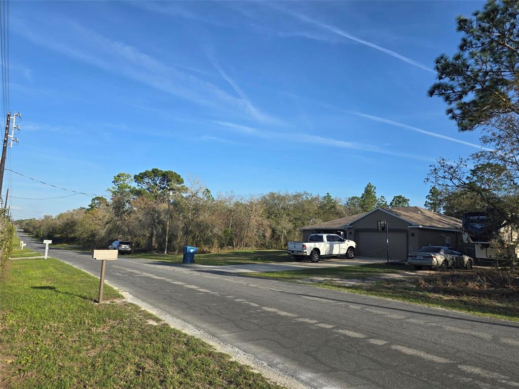 A suburban street view shows a house with a driveway, parked vehicles, and surrounding trees — 13070 QUIGLEY AVENUE, WEEKI WACHEE, FL