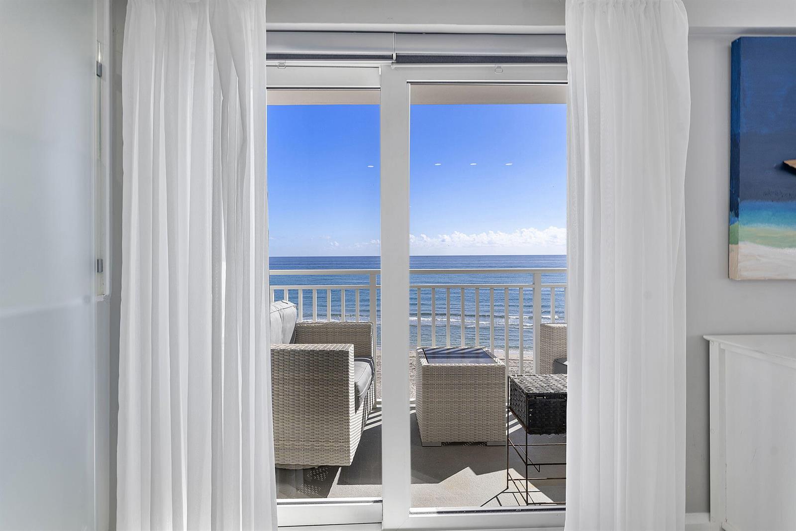 A view through sliding glass doors reveals a balcony with wicker furniture overlooking the ocean — 4505 S Ocean Boulevard # 307, Highland Beach FL 33487, HIGHLAND BEACH, FL