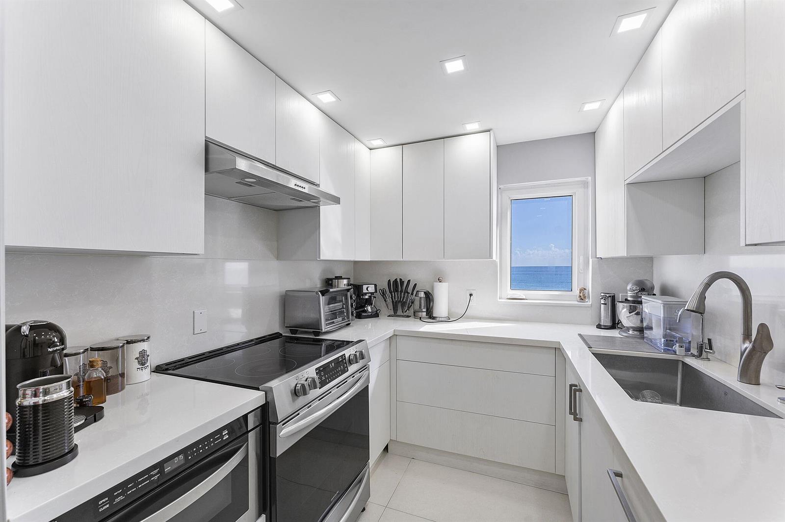 A modern white kitchen features stainless steel appliances, quartz countertops, and a view of the ocean — 4505 S Ocean Boulevard # 307, Highland Beach FL 33487, HIGHLAND BEACH, FL