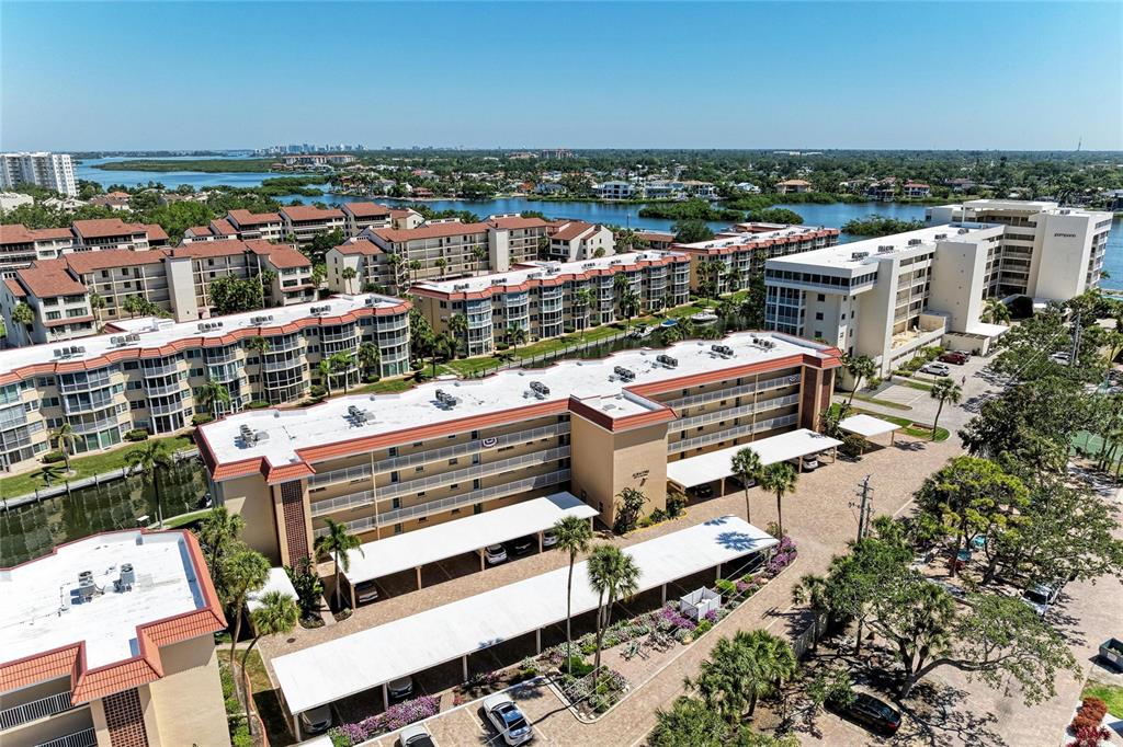 An aerial view shows multiple multi-story apartment buildings with covered parking lots and surrounding greenery — 1257 S PORTOFINO DRIVE UNIT 104, SARASOTA, FL