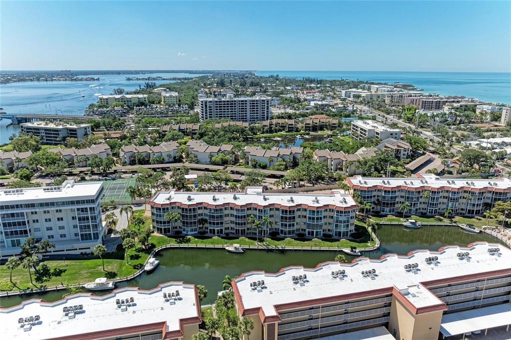 An aerial view shows multiple multi-story apartment buildings situated along a canal near the ocean — 1257 S PORTOFINO DRIVE UNIT 104, SARASOTA, FL