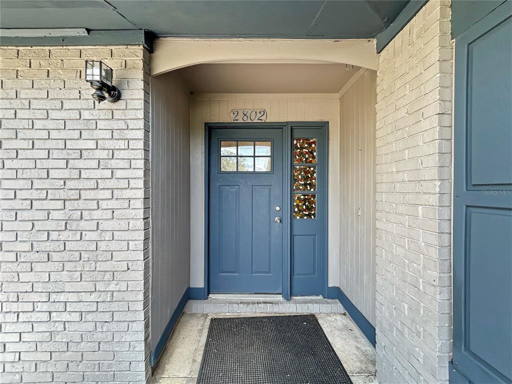 A blue front door with a stained glass sidelight is set within a brick entryway — 2802 CHRISTIE LANE, LAKELAND, FL