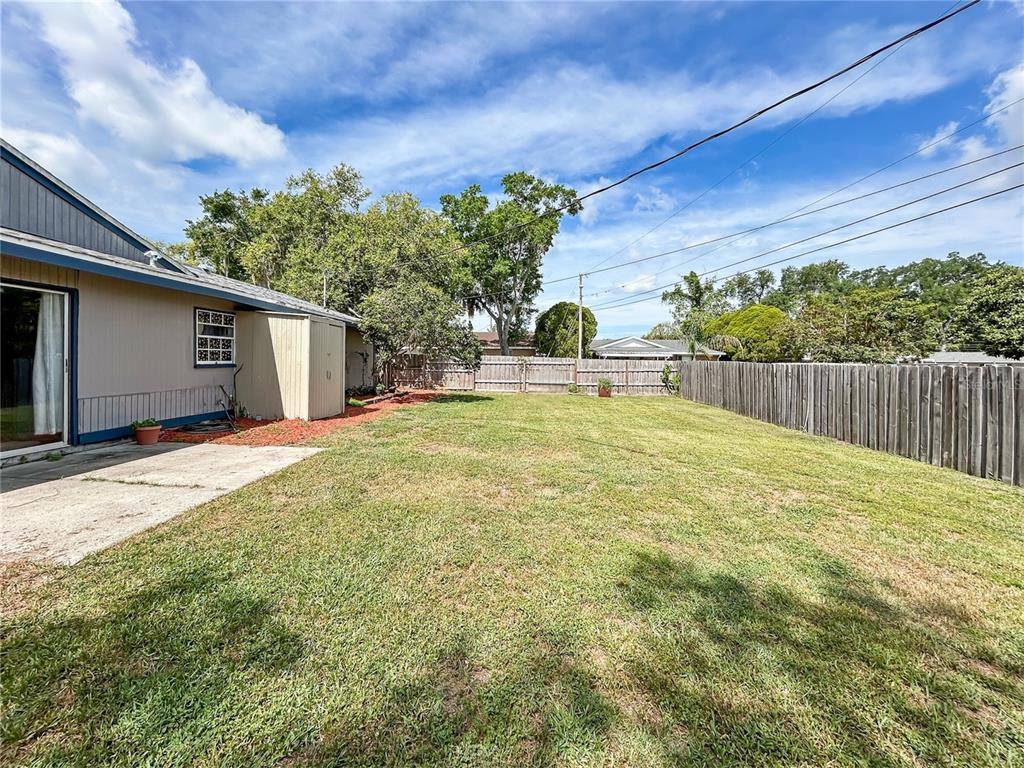 A backyard features a concrete patio, a storage shed, and a wooden privacy fence — 2802 CHRISTIE LANE, LAKELAND, FL