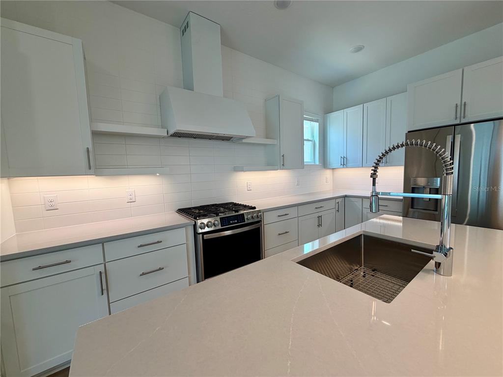 A modern kitchen features white cabinetry, quartz countertops, a stainless steel range, and a sink — 12438 CLEAR SAPPHIRE DRIVE, WINTER GARDEN, FL