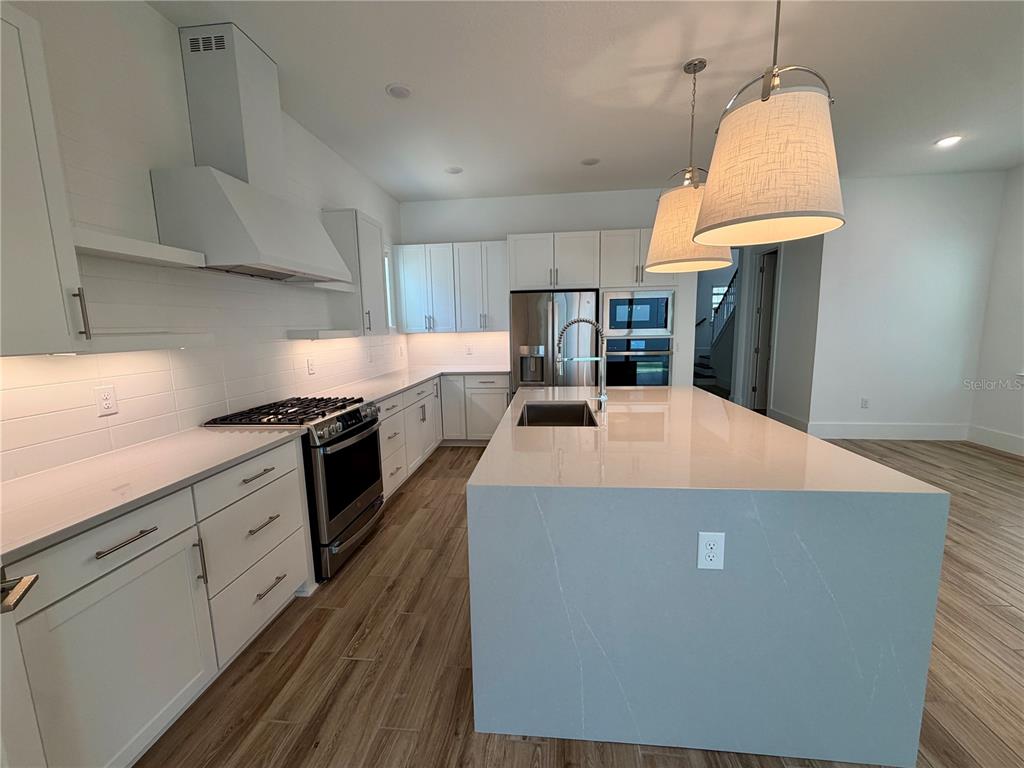A modern kitchen features white cabinetry, a large waterfall island, and wood-look flooring — 12438 CLEAR SAPPHIRE DRIVE, WINTER GARDEN, FL