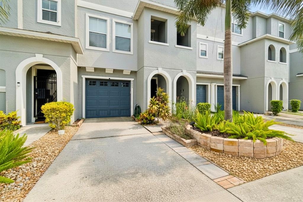 A multi-story townhouse exterior with a blue garage door, arched entryways, and a palm tree — 4853 TUSCAN LOON DRIVE, TAMPA, FL
