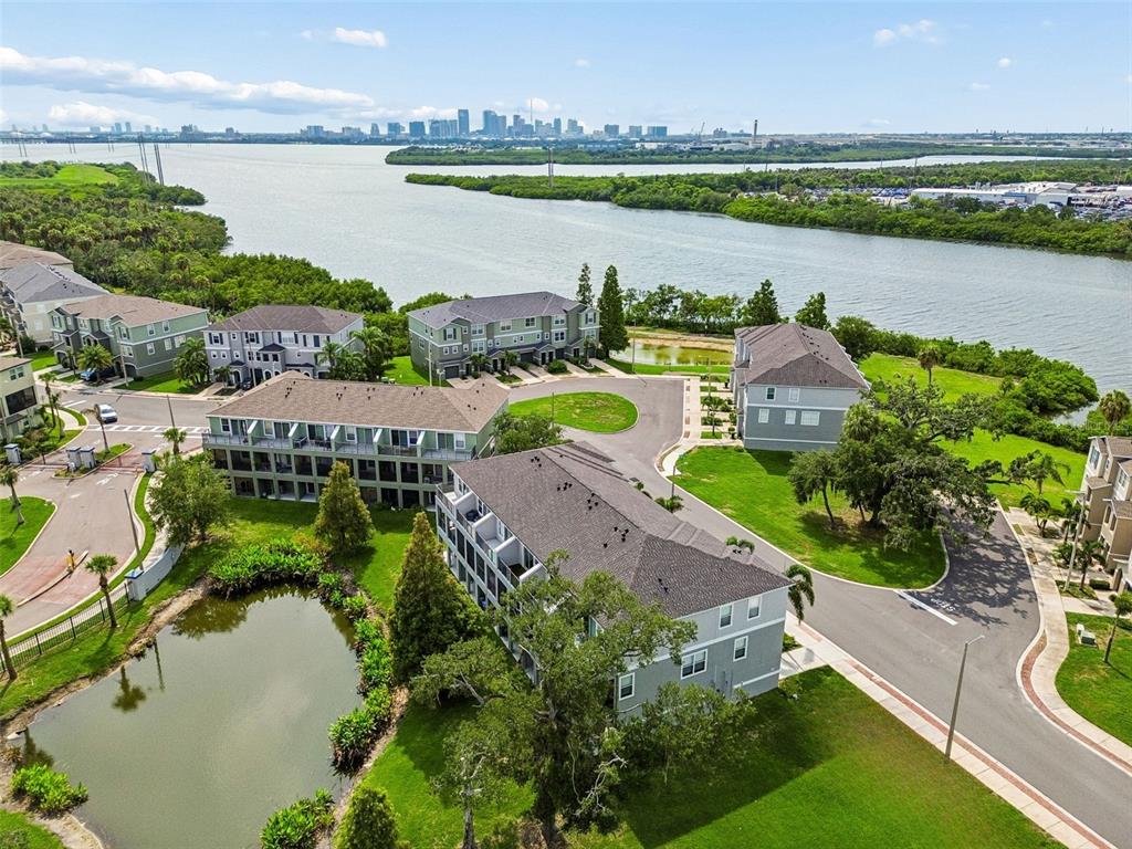 An aerial view shows multi-story residential buildings near a pond and a large bay — 4853 TUSCAN LOON DRIVE, TAMPA, FL