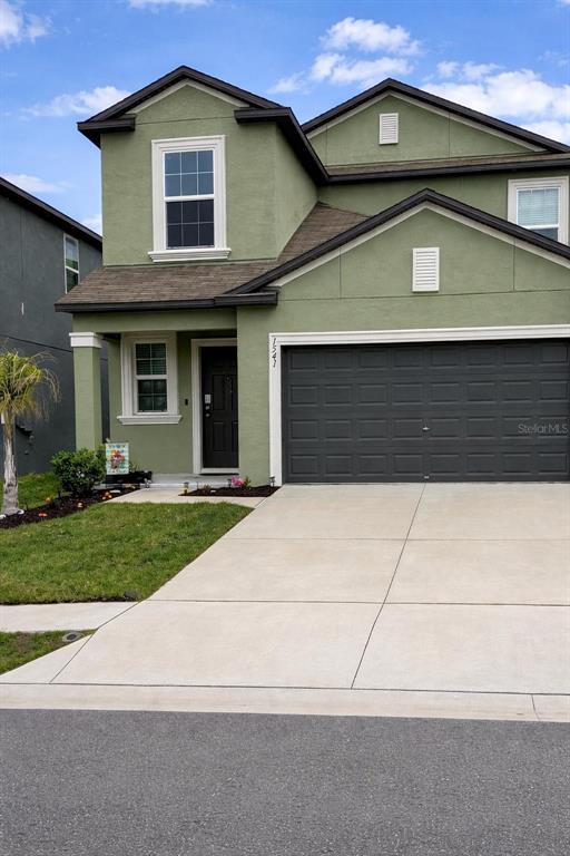 A two-story house with green stucco siding, a dark garage door, and a concrete driveway — 1541 LANDMARK DRIVE, LAKELAND, FL