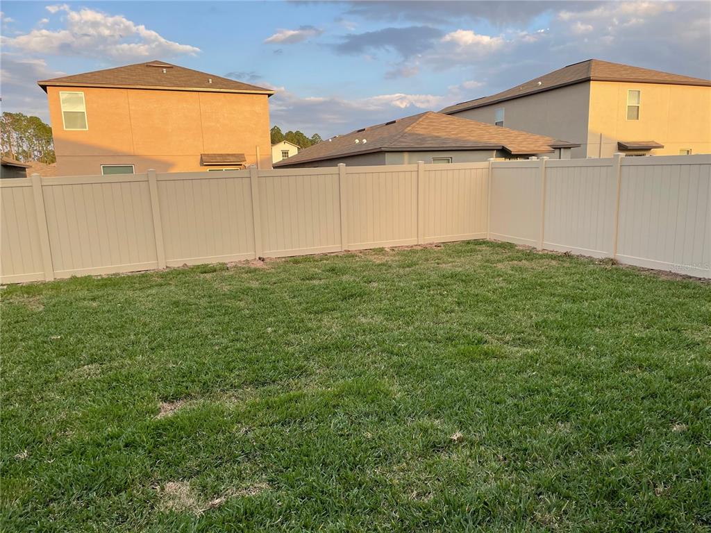 A grassy backyard is enclosed by a tall, tan vinyl privacy fence — 1541 LANDMARK DRIVE, LAKELAND, FL