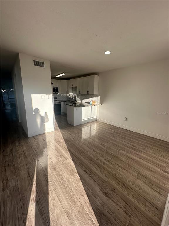 An open-concept kitchen with white cabinets and wood-look flooring flows into a living area — 5064 DOWNING STREET UNIT 4, ORLANDO, FL