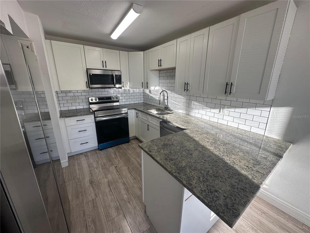 A kitchen features white cabinets, granite countertops, a stainless steel microwave, and subway tile backsplash — 5064 DOWNING STREET UNIT 4, ORLANDO, FL