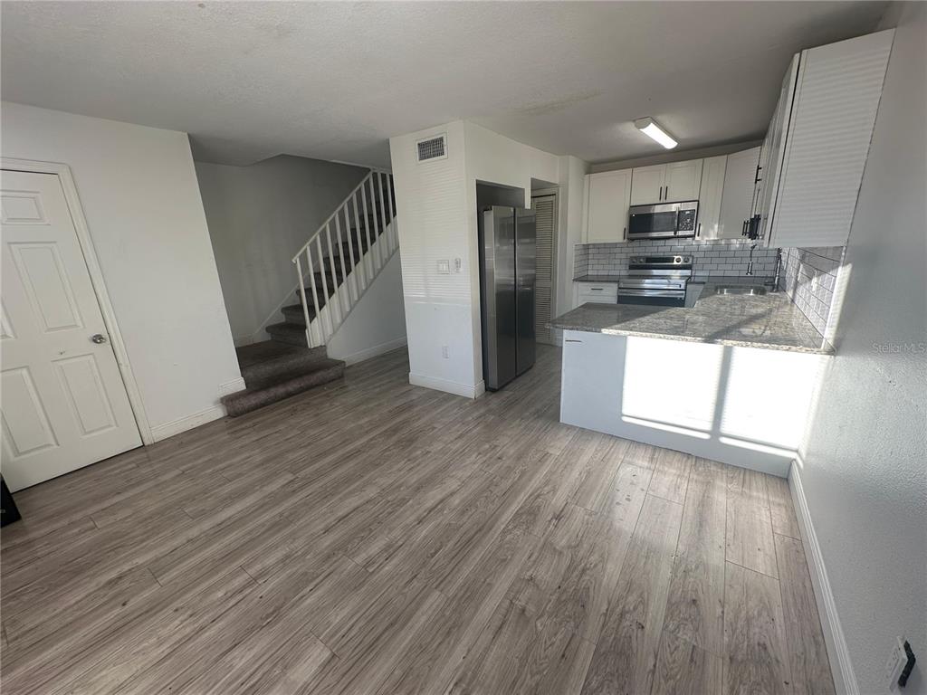 A kitchen with white cabinets and stainless steel appliances overlooks a room with wood flooring — 5064 DOWNING STREET UNIT 4, ORLANDO, FL