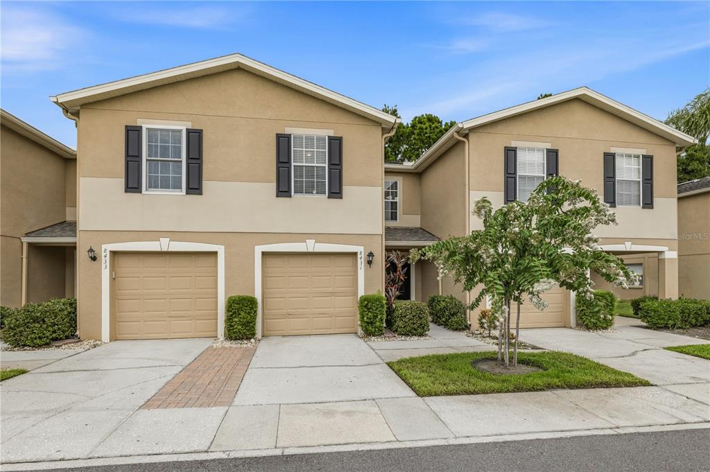 A two-story townhouse exterior features tan stucco walls, dark shutters, and three garage doors — 8431 EDGEWATER PLACE BOULEVARD, TAMPA, FL