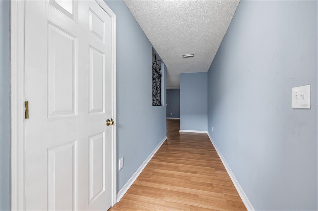 A hallway with light blue walls, wood-look flooring, and a white door on the left — 8431 EDGEWATER PLACE BOULEVARD, TAMPA, FL