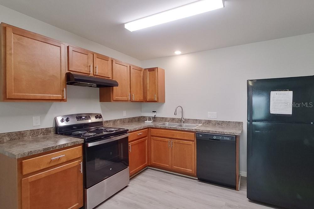 A kitchen features wooden cabinets, stainless steel appliances, a black dishwasher, and laminate countertops — 3214 65TH STREET W, LEHIGH ACRES, FL