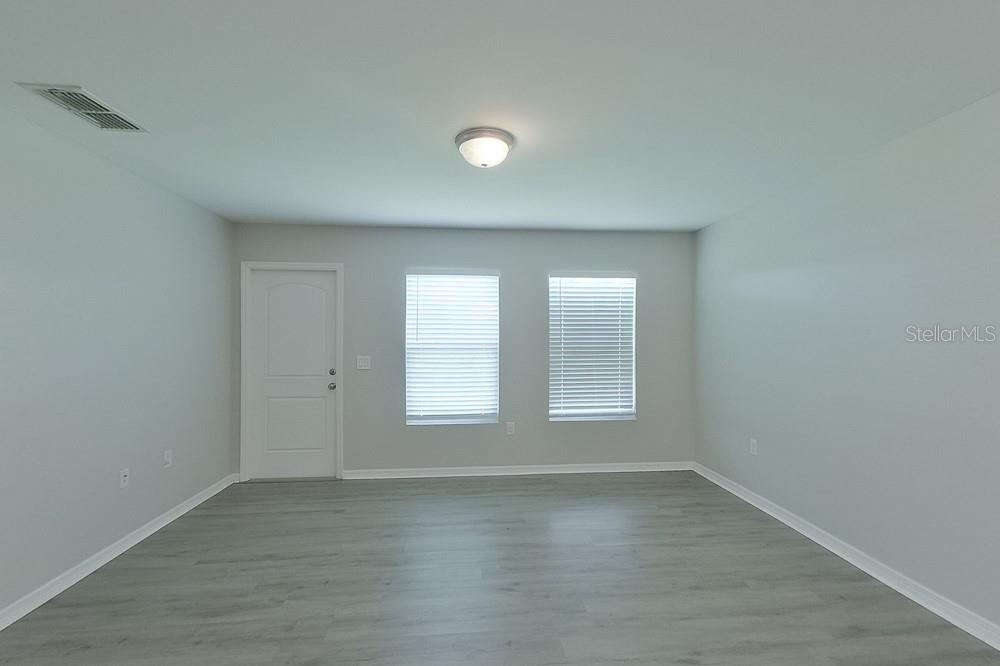 An empty room with light gray walls, wood-look flooring, two windows, and a white door — 3214 65TH STREET W, LEHIGH ACRES, FL