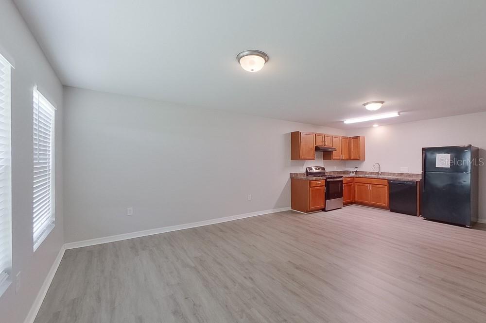An open-concept kitchen with wood cabinets and a black refrigerator sits beside a living area — 3214 65TH STREET W, LEHIGH ACRES, FL