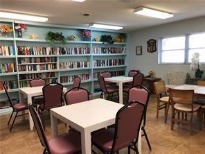 A library or community room features multiple tables, chairs, and floor-to-ceiling bookshelves — 7877 Golf Circle Drive # 211, Margate FL 33063, MARGATE, FL