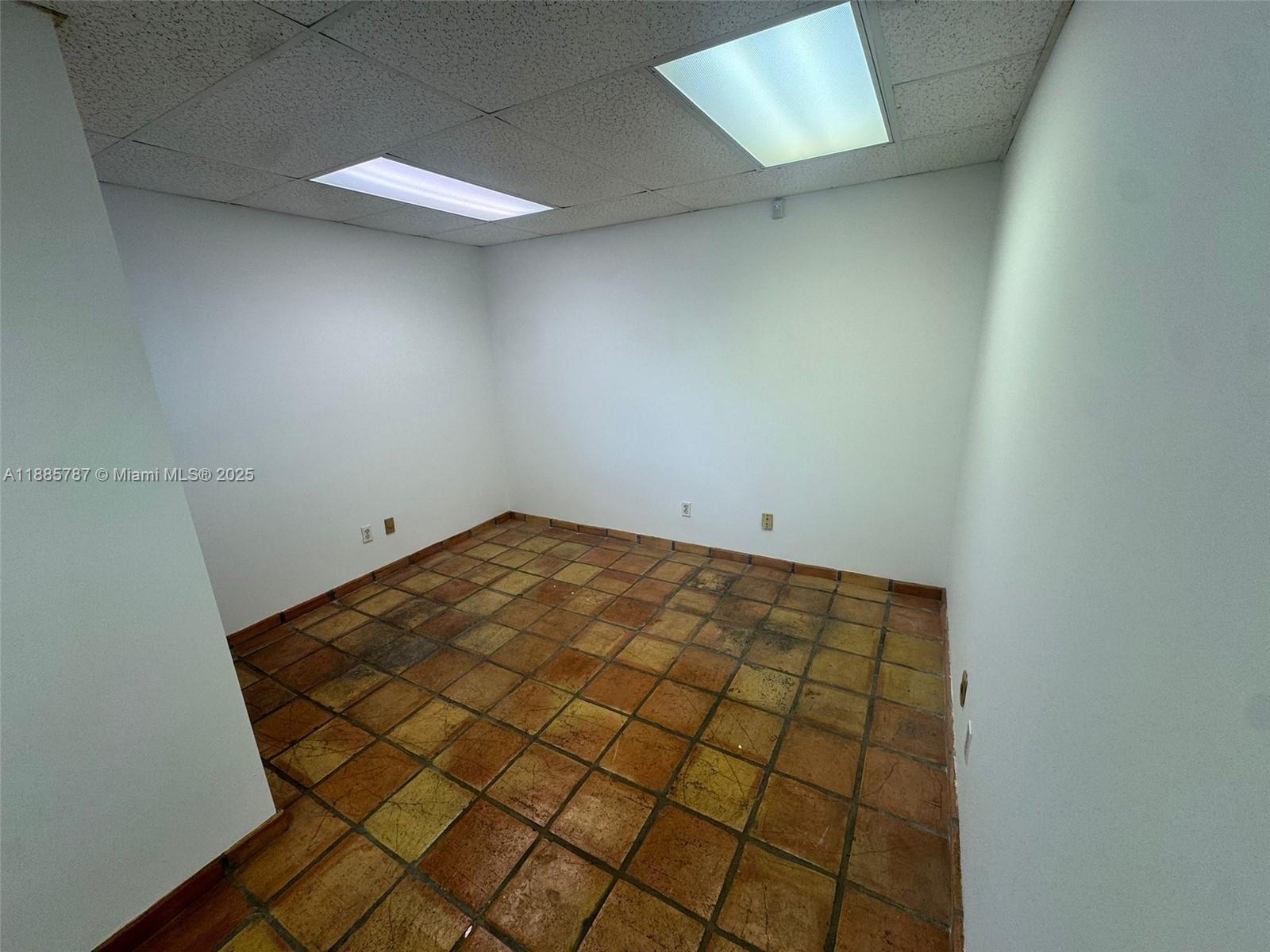 An empty office room features white walls, a drop ceiling with fluorescent lights, and terracotta tiles — 10849 NW 29th St # 10849, Doral FL 33172, DORAL, FL
