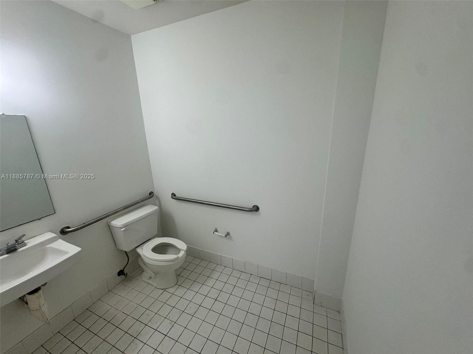 A white-tiled bathroom features a toilet, a sink, and wall-mounted grab bars — 10849 NW 29th St # 10849, Doral FL 33172, DORAL, FL
