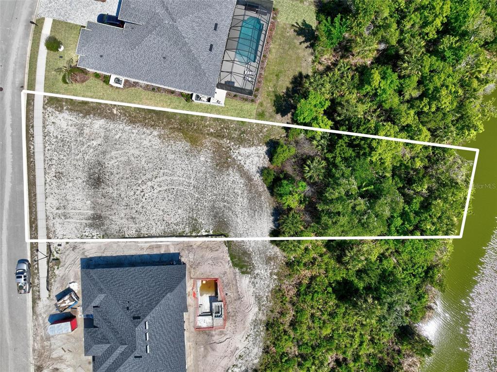 An aerial view shows a vacant residential lot bordered by a road, houses, and woods — 128 N LAKEWALK DRIVE, PALM COAST, FL
