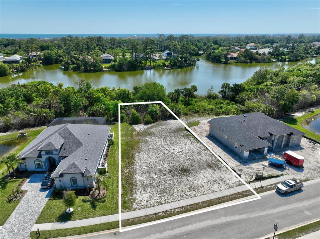An aerial view shows a vacant residential lot situated between two houses near a lake — 128 N LAKEWALK DRIVE, PALM COAST, FL