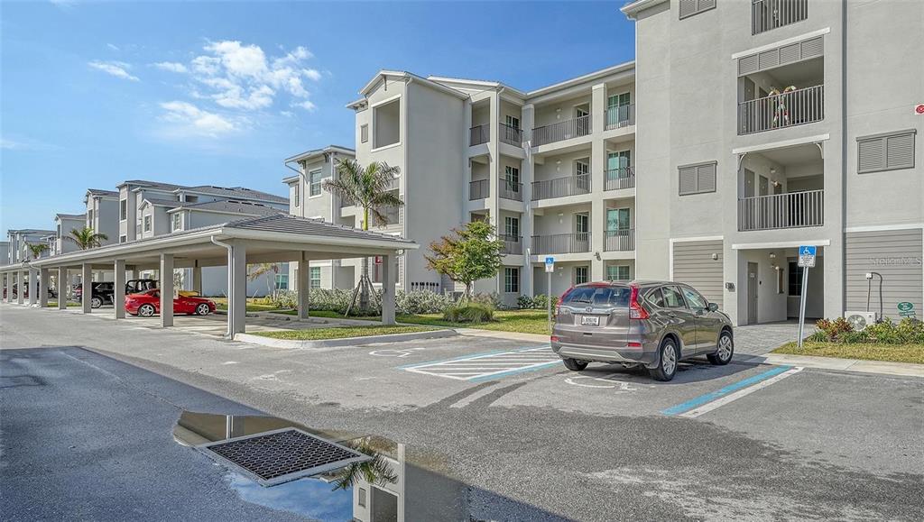 An exterior view of a multi-story apartment building with covered parking and a handicap space — 12180 WELLEN GOLF STREET UNIT 203, VENICE, FL