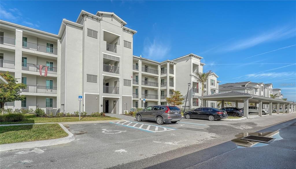 A multi-story apartment building with a parking lot and covered parking spaces in front — 12180 WELLEN GOLF STREET UNIT 203, VENICE, FL
