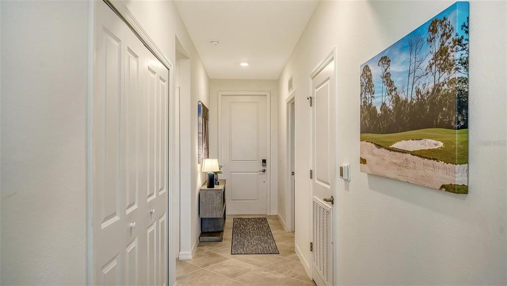 A hallway with tile flooring, white doors, a small console table, and wall art — 12180 WELLEN GOLF STREET UNIT 203, VENICE, FL