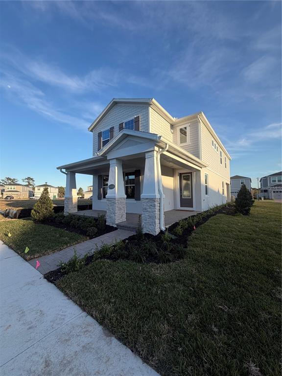 A two-story house with light siding, a stone-columned front porch, and a landscaped yard — 1389 LUMPINI STREET, ST CLOUD, FL