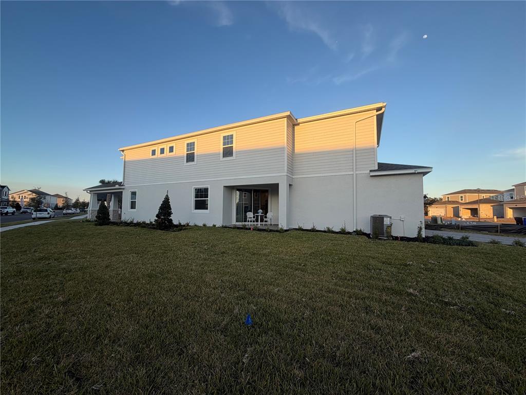 The exterior of a two-story house features light-colored siding, a small patio, and a grassy yard — 1389 LUMPINI STREET, ST CLOUD, FL